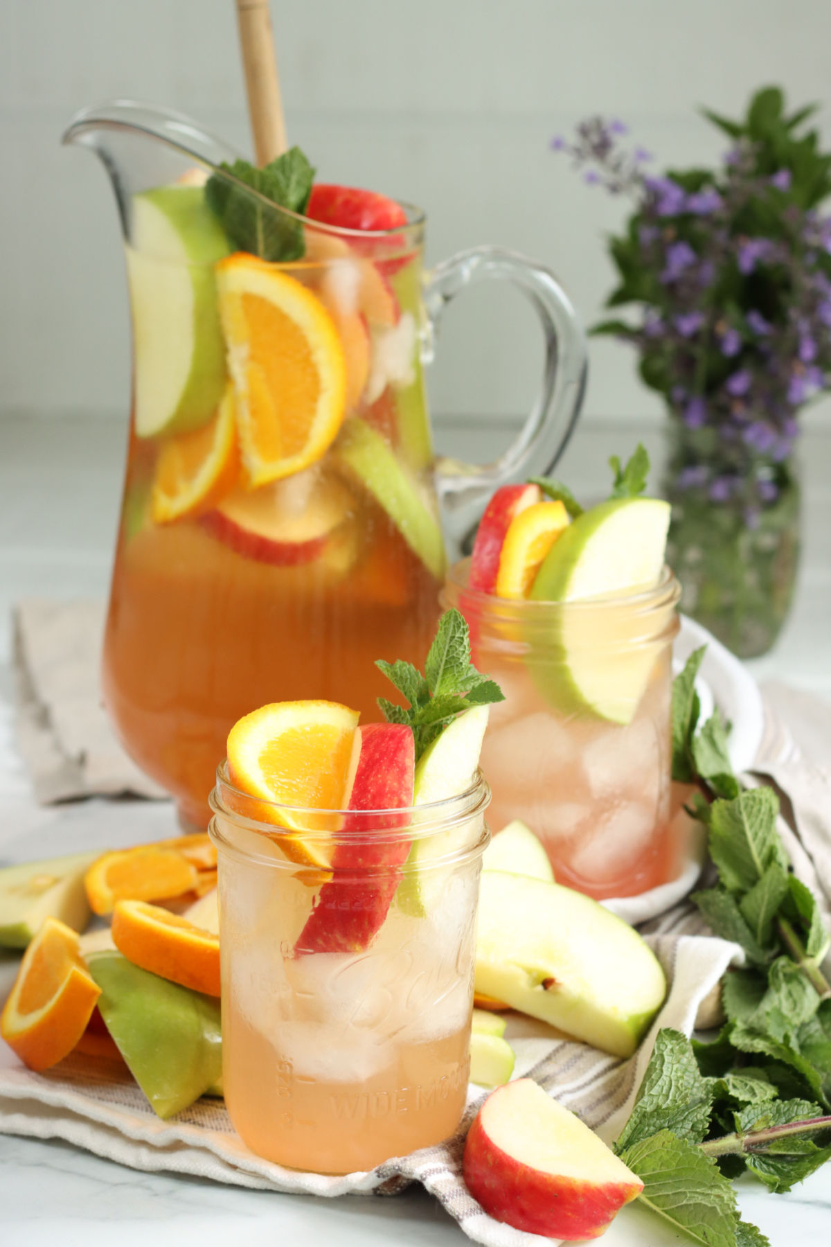 Mason jars with white sangria, ice cubes, red and green apple slices, orange slices, fresh mint.