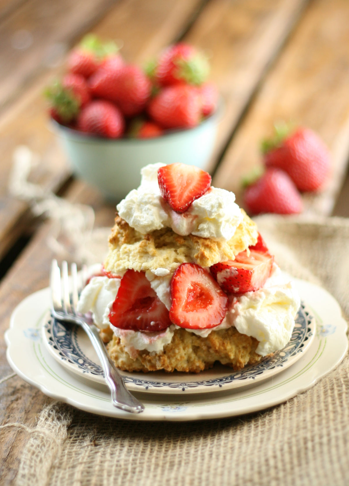 Shortcake biscuit cut in half with slices of strawberries and whipped cream on small white plate.