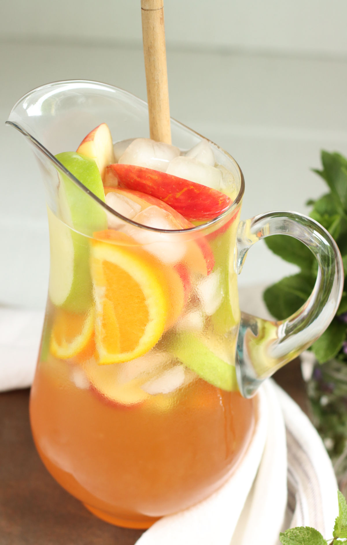 Glass pouring pitcher with white sangria, red and green apples, orange slices.