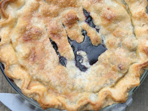 Blueberry pie with golden browned pie crust in clear glass pie dish.