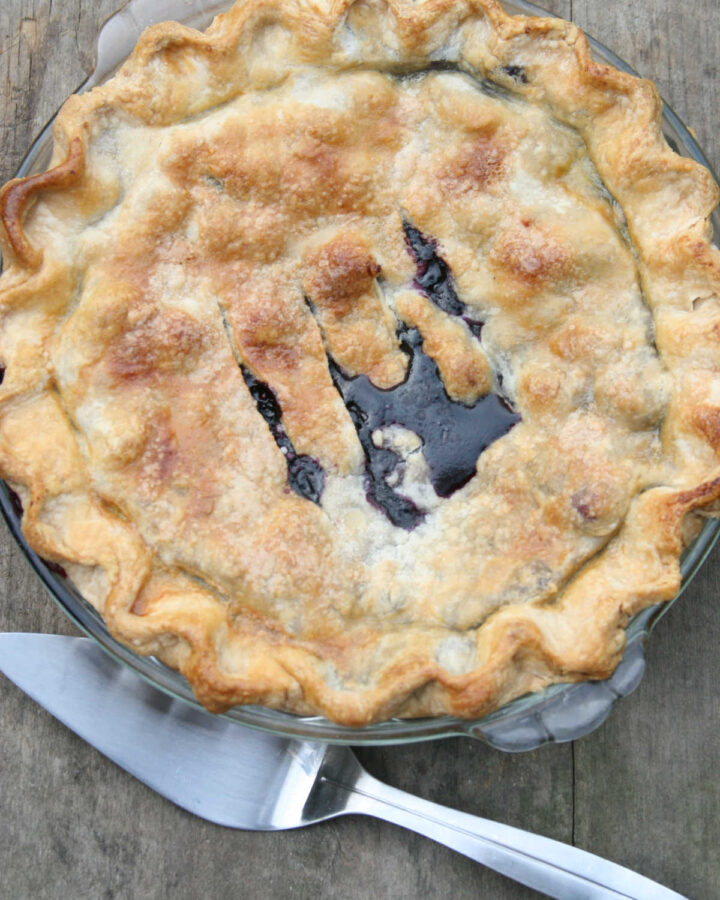 Blueberry pie with golden browned pie crust in clear glass pie dish.