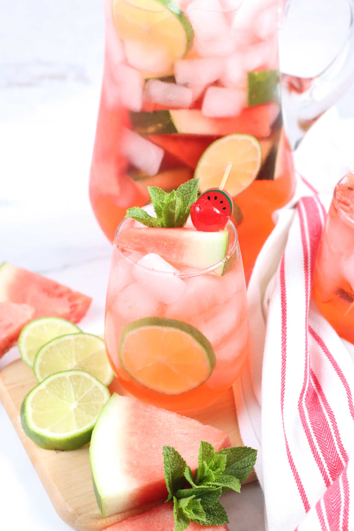 Clear pouring pitcher and stemless wine glass with watermelon sangria, ice cubes, fresh mint.