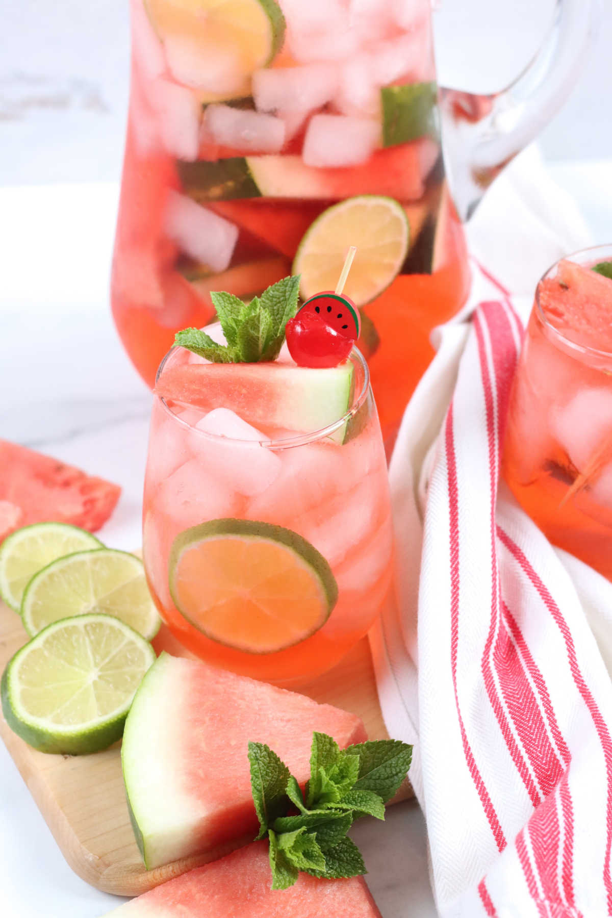 Watermelon sangria in glass pouring pitcher and stemless wine glass on wooden cutting board.