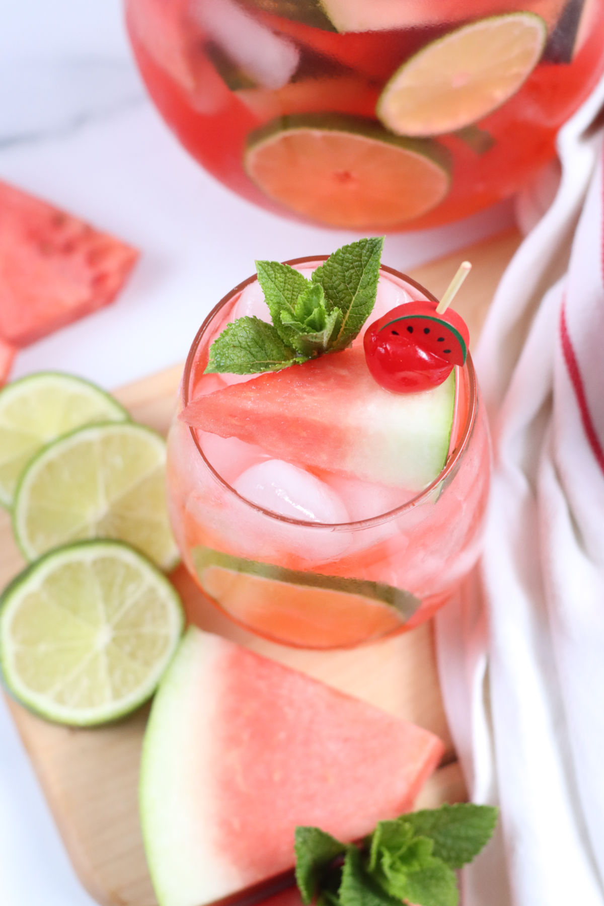 Overhead shot stemless wine glass with watermelon sangria, ice cubes, lime slices.
