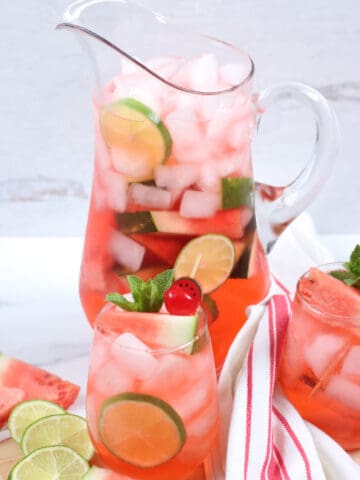 Glass pouring pitcher of watermelon sangria, stemless wine glasses.