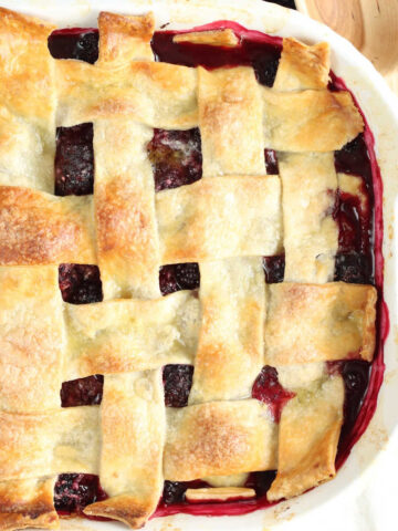 Blackberry cobbler with pie crust in white baking dish, fresh blackberries around.