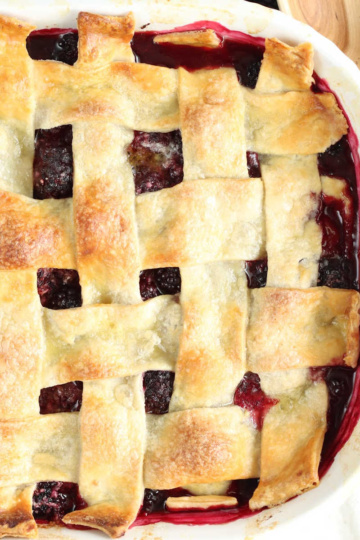 Blackberry cobbler with pie crust in white baking dish, fresh blackberries around.