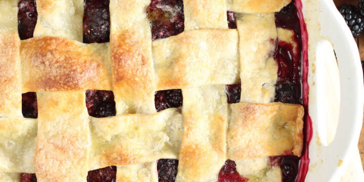 Blackberry cobbler with pie crust in white baking dish, fresh blackberries around.