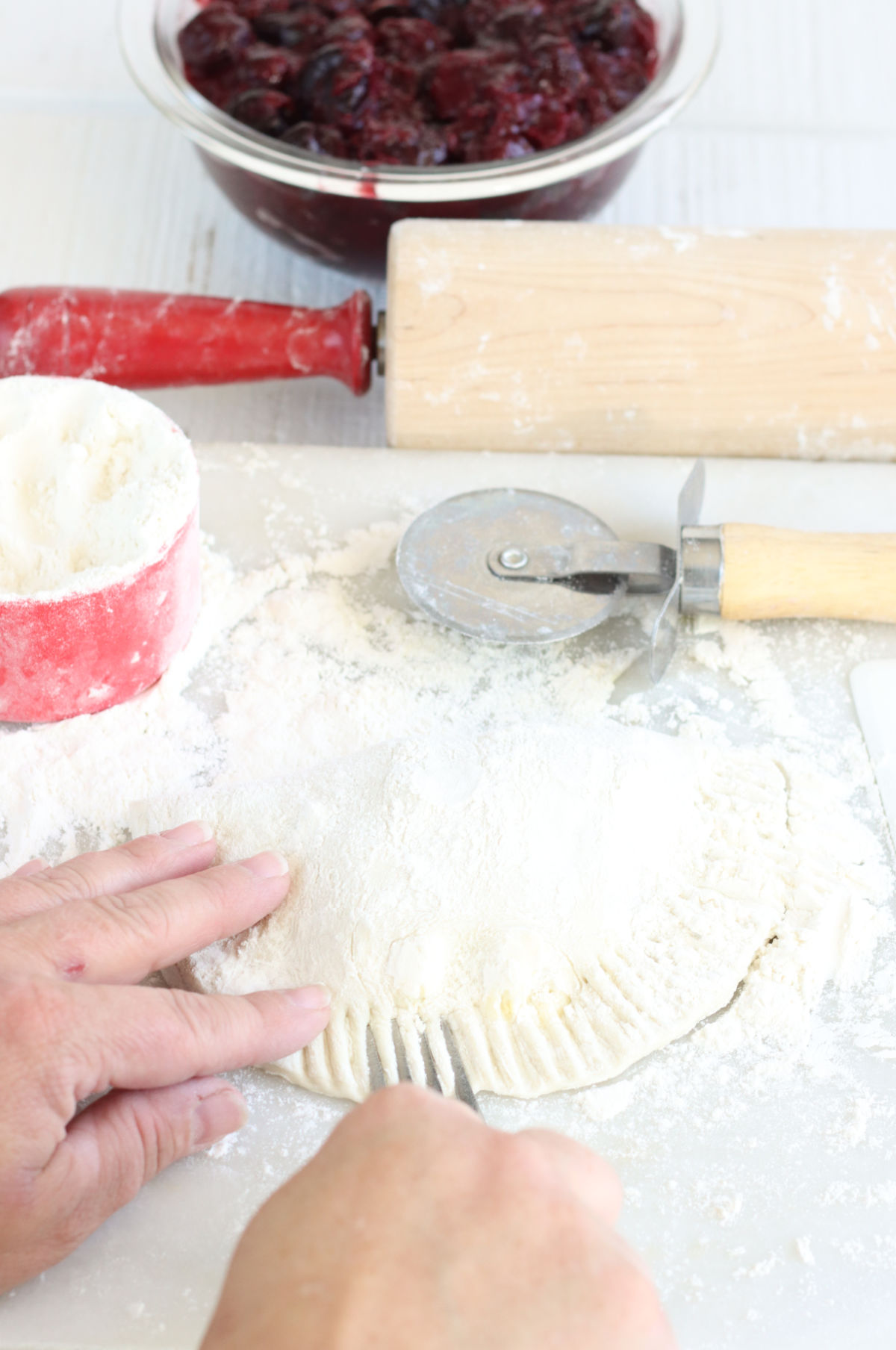 Assembling hand pies on white marble, pressing edges with fork.