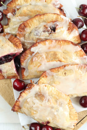 Cherry hand pies on wooden cutting board, fresh cherries around.