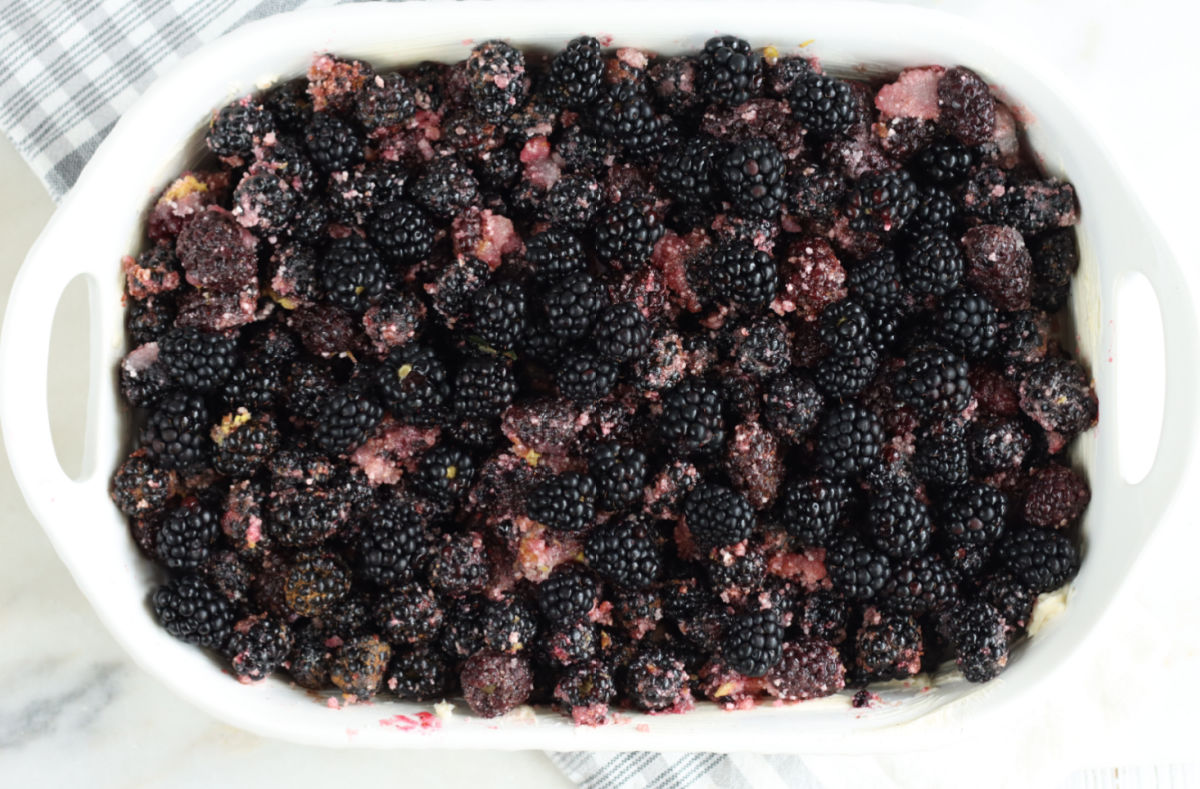 Blackberries mixed with sugar in white rectangle baking dish.