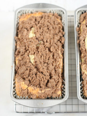Coffee cake with crumb topping in metal loaf pans on metal baking rack.