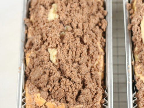 Coffee cake with crumb topping in metal loaf pans on metal baking rack.
