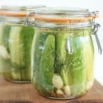 Glass jar with clasp lids and rubber seals filled with pickle spears on wooden cutting board.