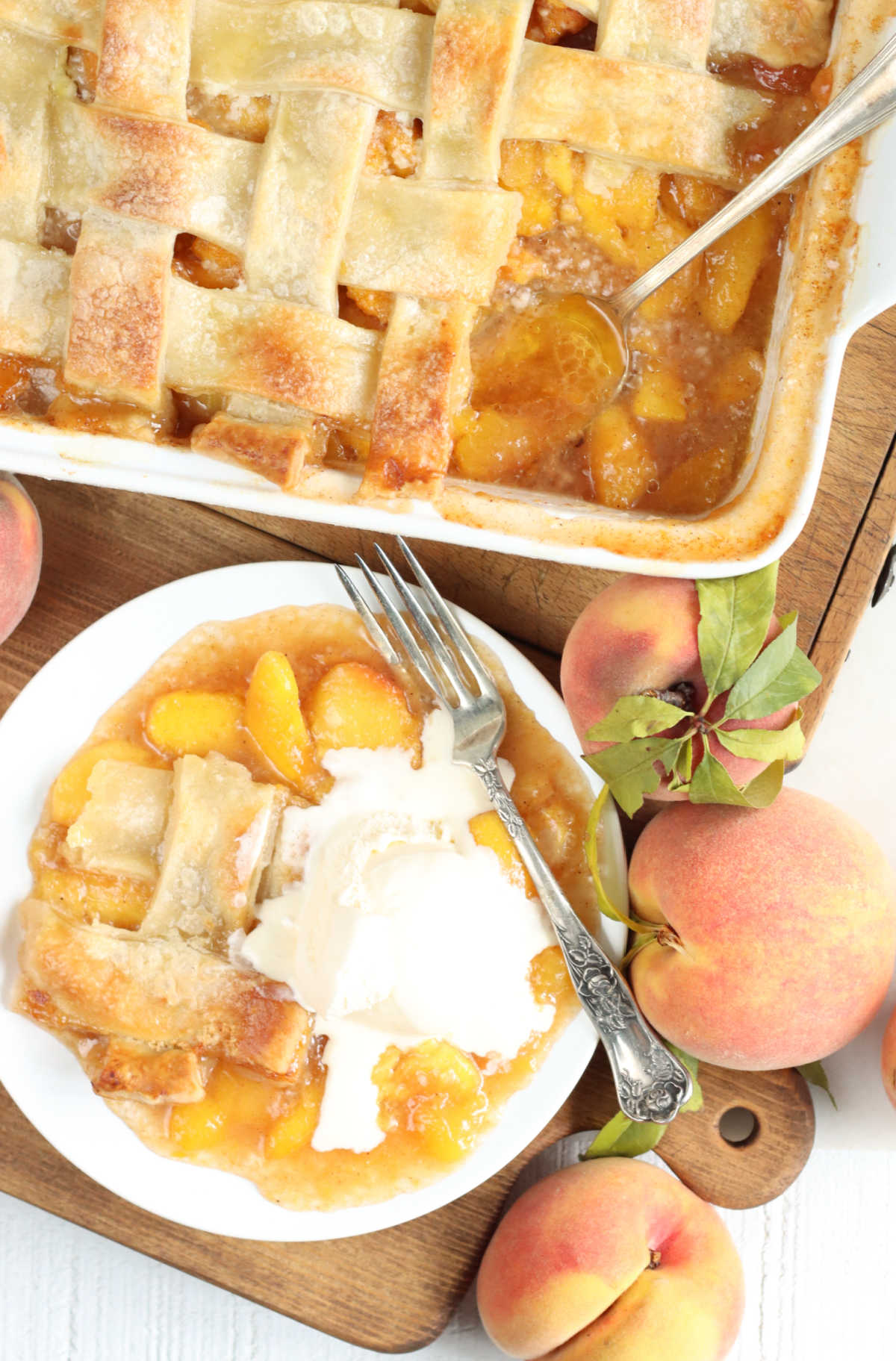 Peach cobbler with pie crust on small white plate with scoop of vanilla ice cream and fork.