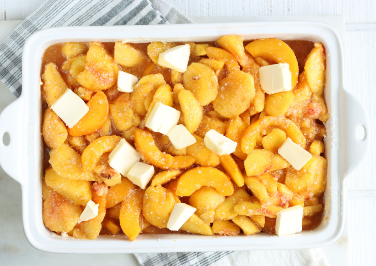 Peaches inside a white rectangle baking dish topped with butter.