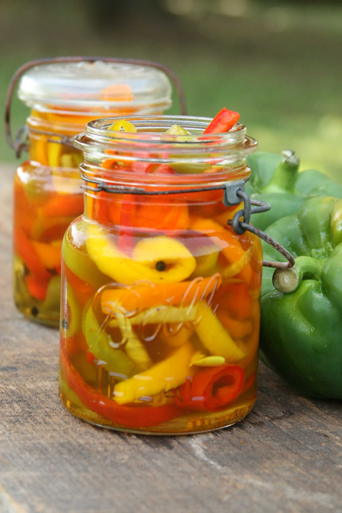 Vintage Mason jar with multi colored pickled bell peppers, sitting outside on reclaimed wood board.