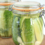 Jars of dill pickle spears on wooden cutting board.