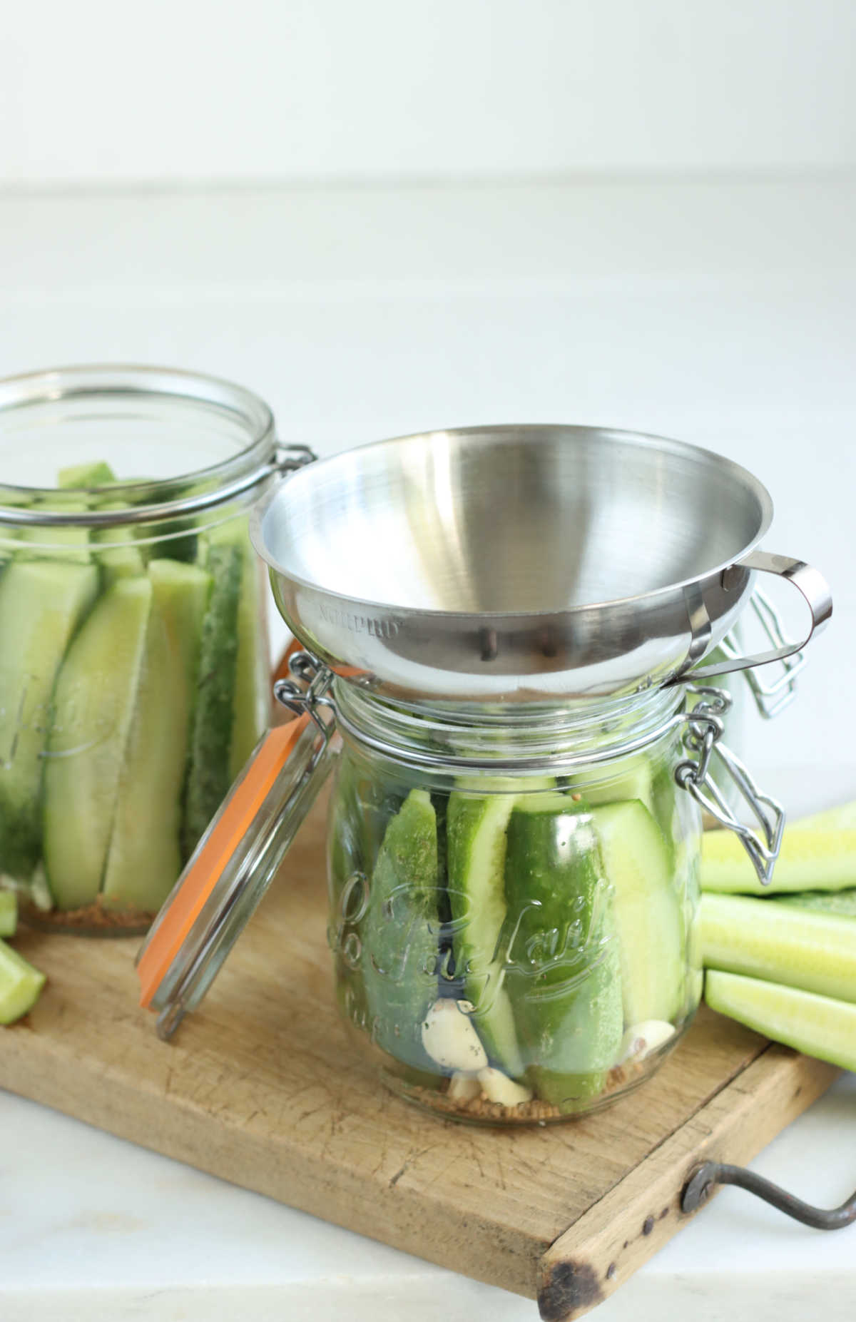 Glass jars with cucumber spears pouring pickling brine over top in measuring cup.
