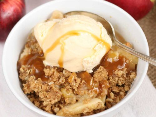Apple crumble topped with vanilla ice cream, caramel sauce, spoon in small white bowl.