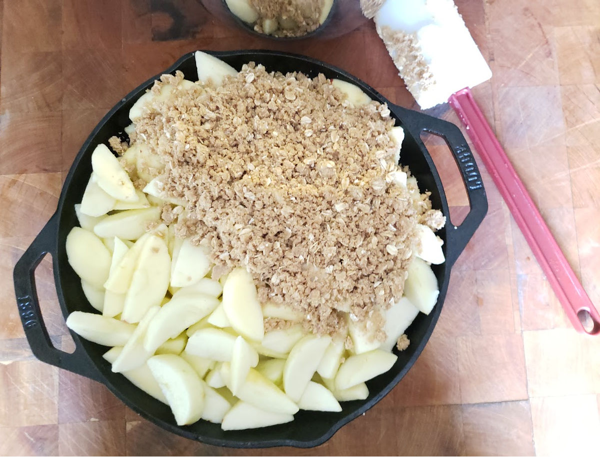 Apple crumble with oatmeal topping in dual handle cast iron skillet on butcher block.