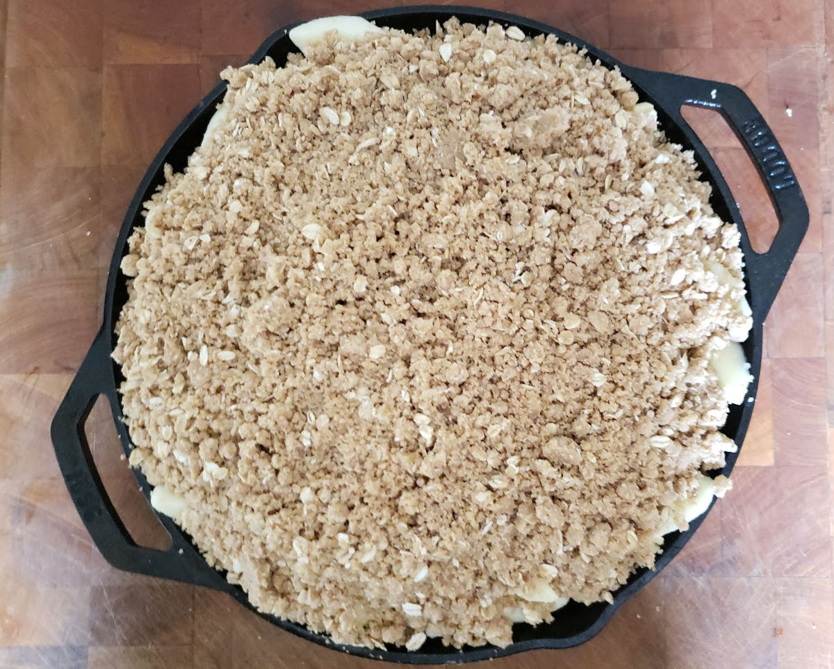 Unbaked apple crumble in dual handle cast iron skillet on butcher block.