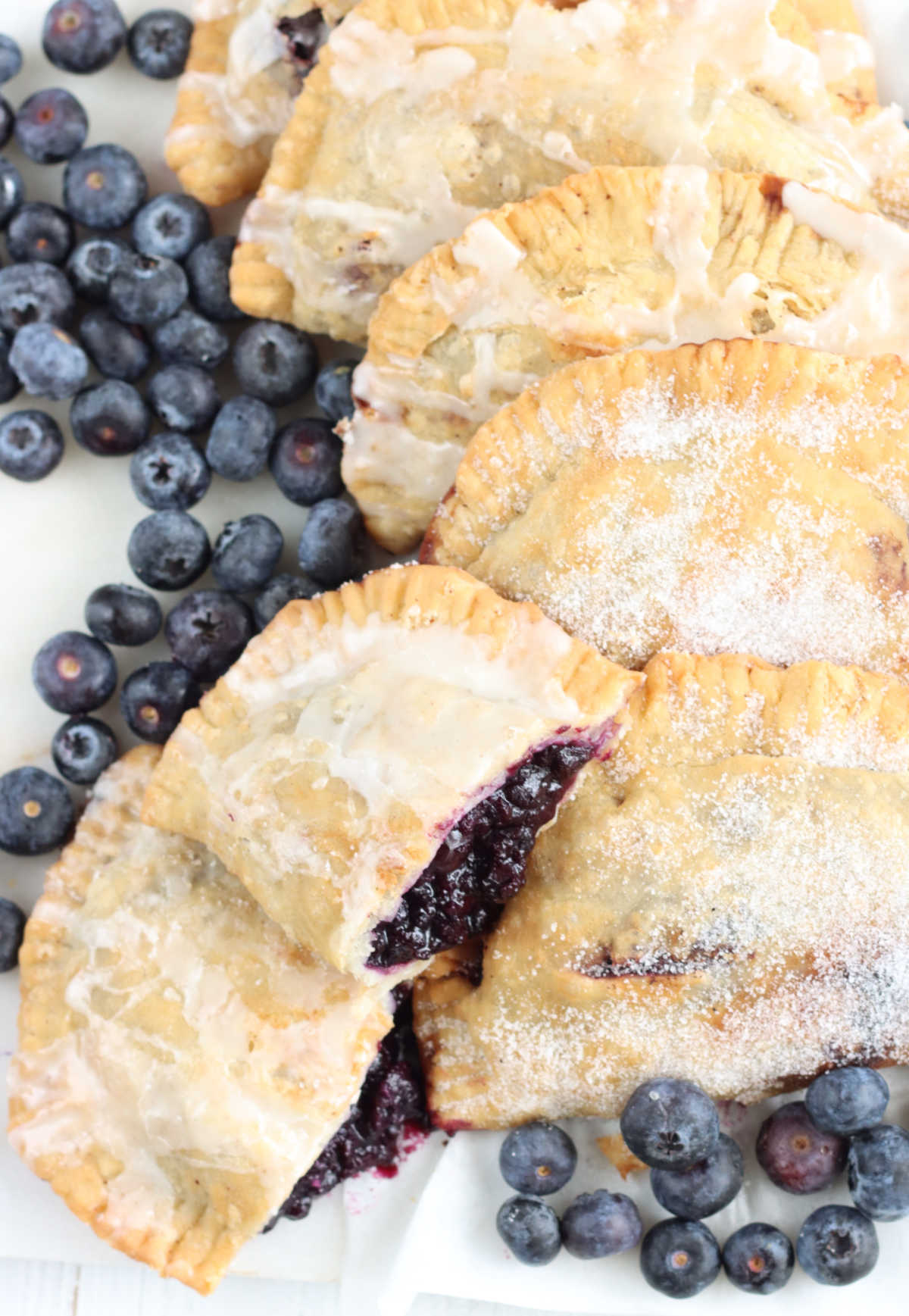 Hand pies on white marble, one cut in half with blueberry pie filling showing.