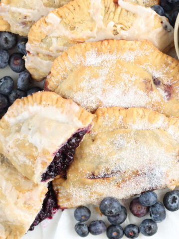 Blueberry hand pies on white marble, loose fresh blueberries around.