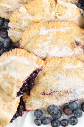 Blueberry hand pies on white marble, loose fresh blueberries around.