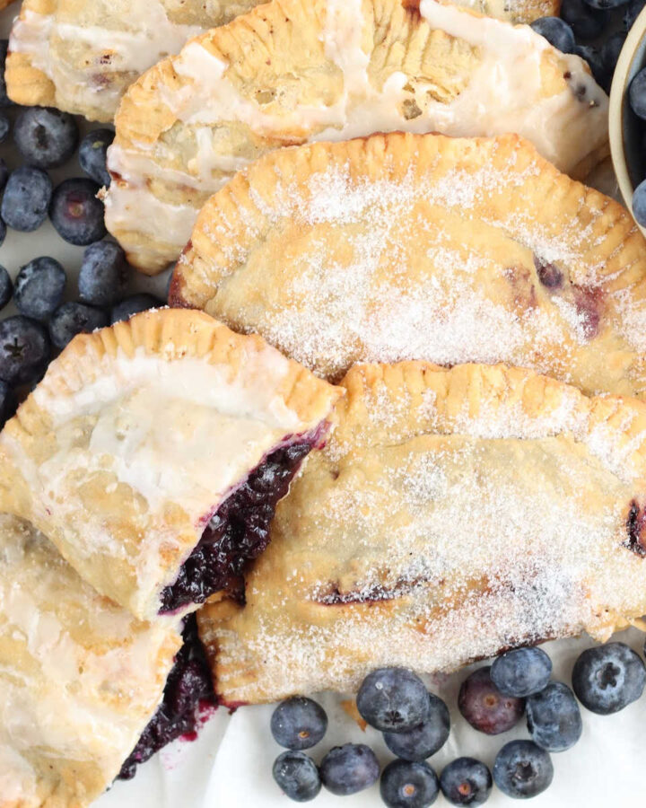 Blueberry hand pies on white marble, loose fresh blueberries around.