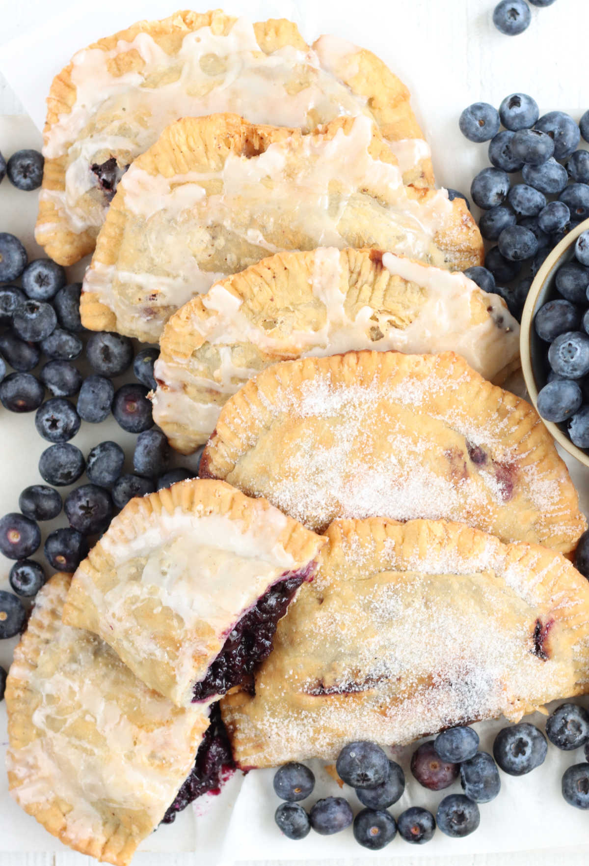 Hand pies on white marble with fresh blueberries around.