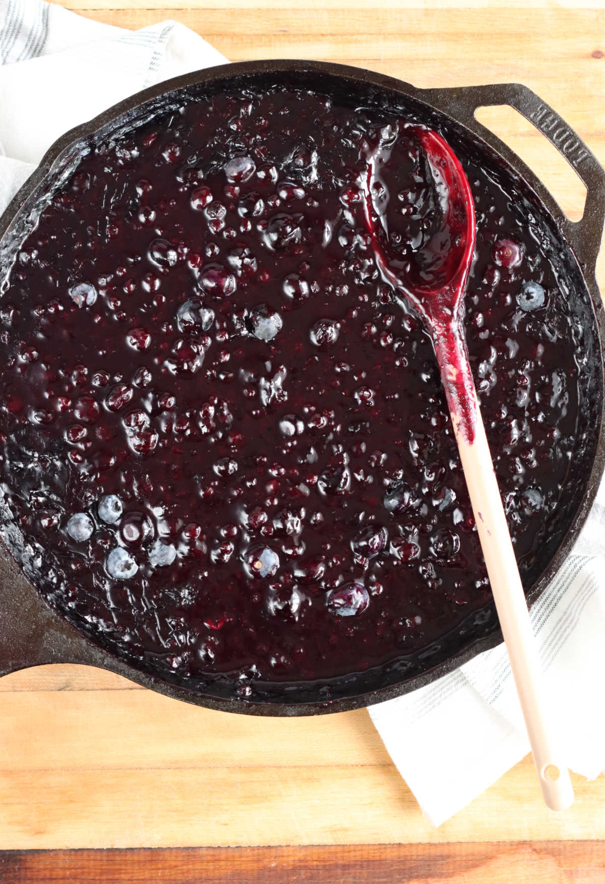 Blueberry pie filling in large cast iron skillet with spoon in skillet on butcher block.