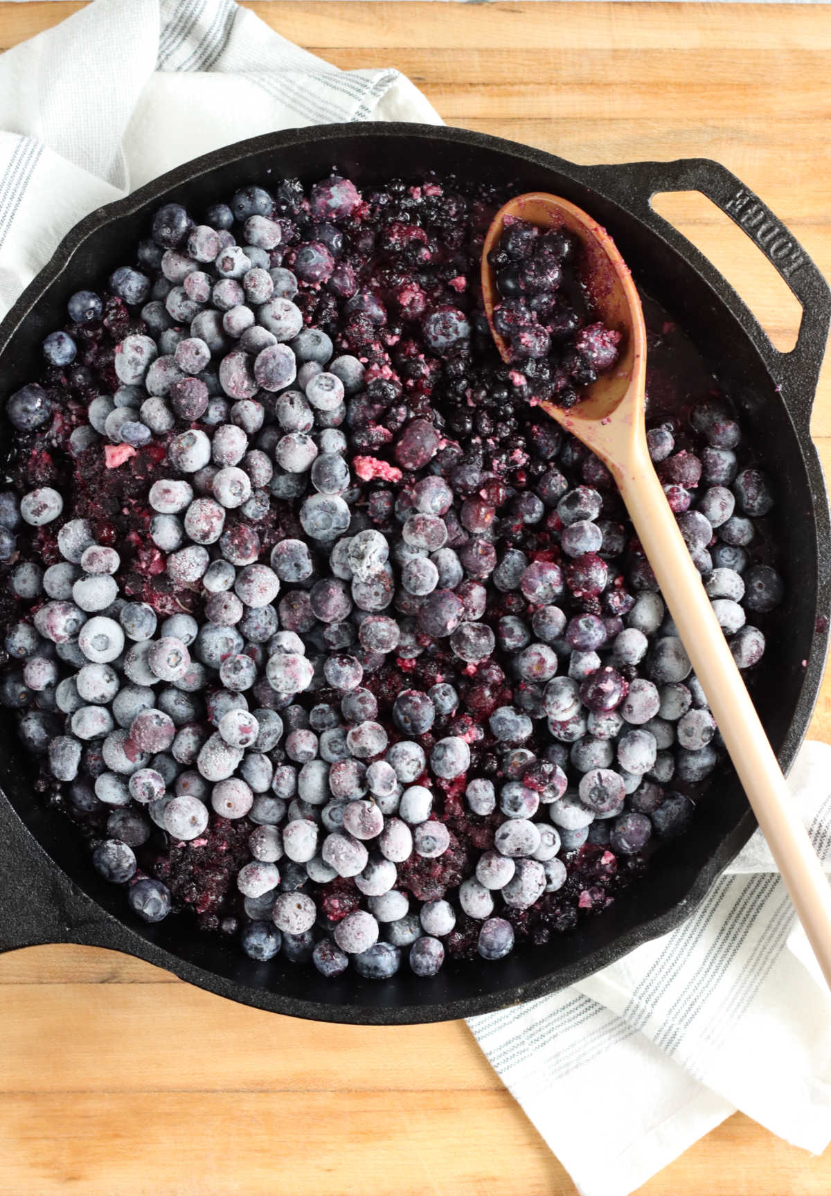 Large cast iron skillet with frozen blueberries and spoon on butcher block.