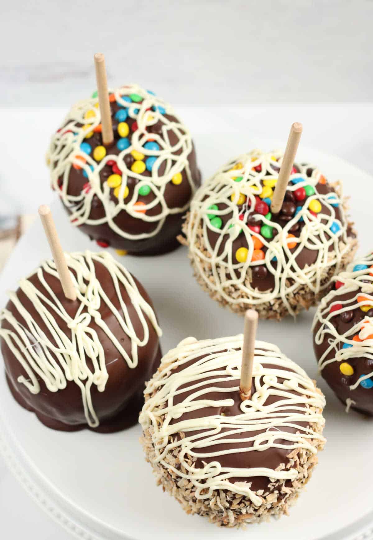 Caramel apples on white footed cake dish with chocolate and candies.