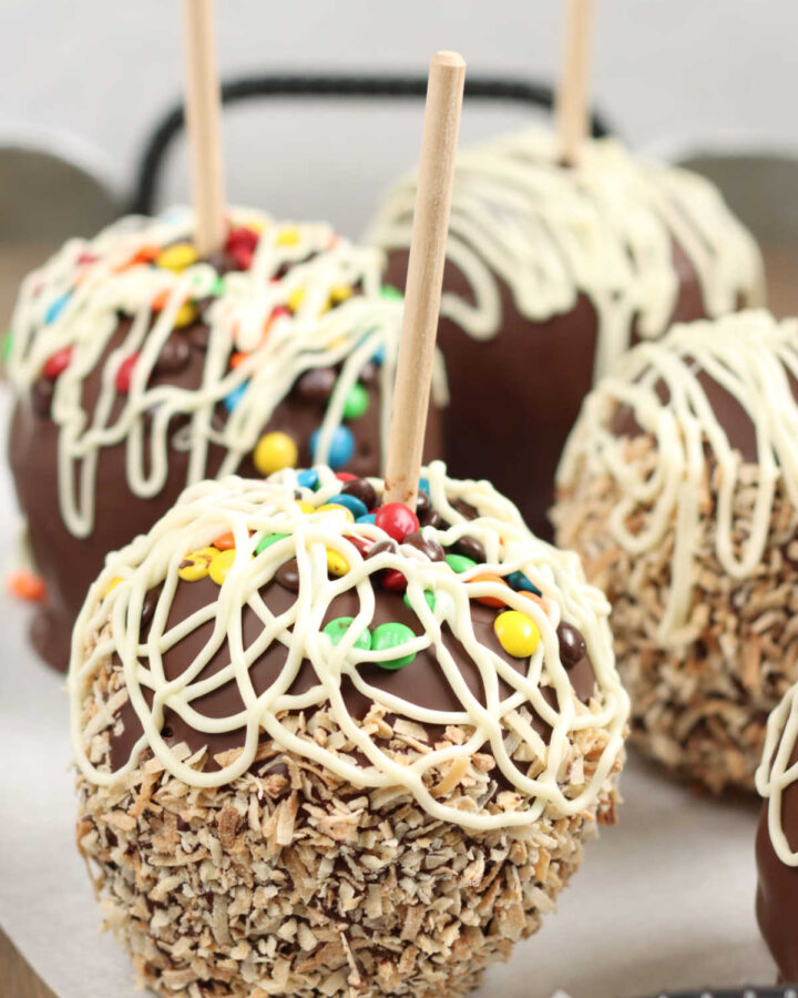 Caramel chocolate apples with toasted coconut and candies on serving tray.