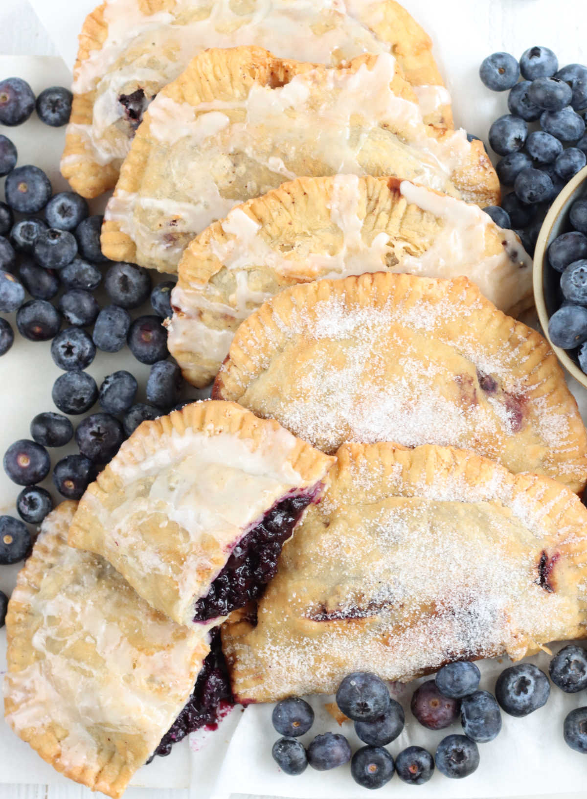 Blueberry hand pies on white marble with fresh blueberries around.