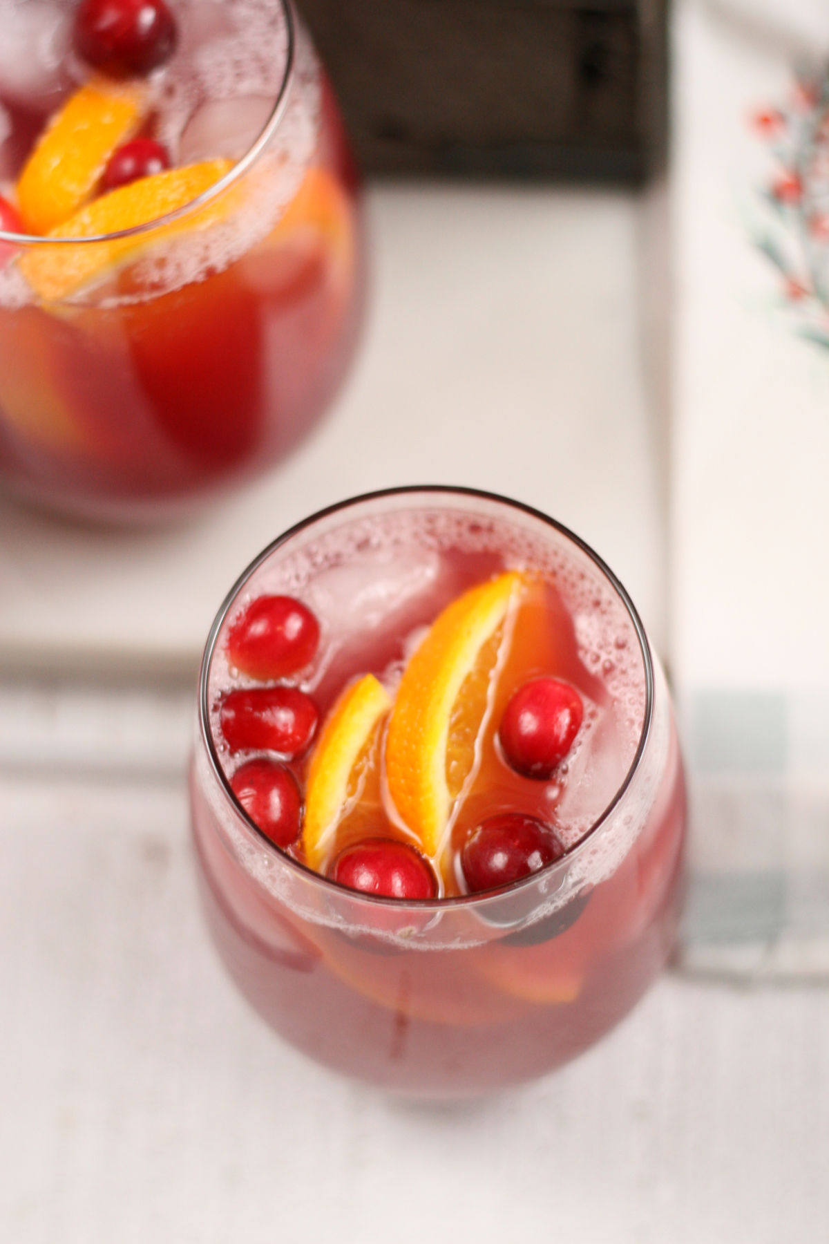 Stemless wine glass with holiday punch, ice cubes, cranberries and orange slices.