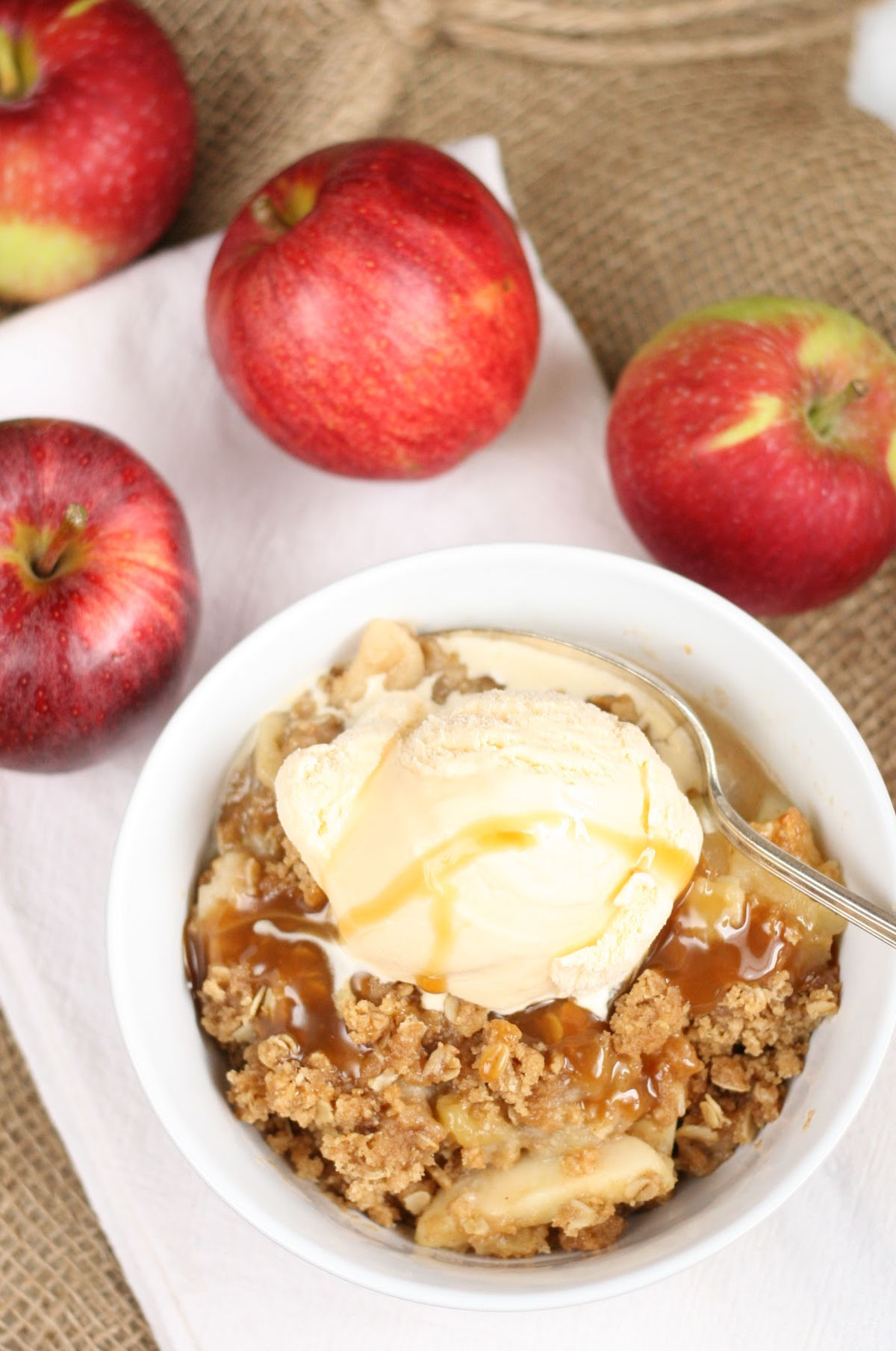 Apple crisp with oatmeal topping in small white bowl, topped with vanilla ice cream.