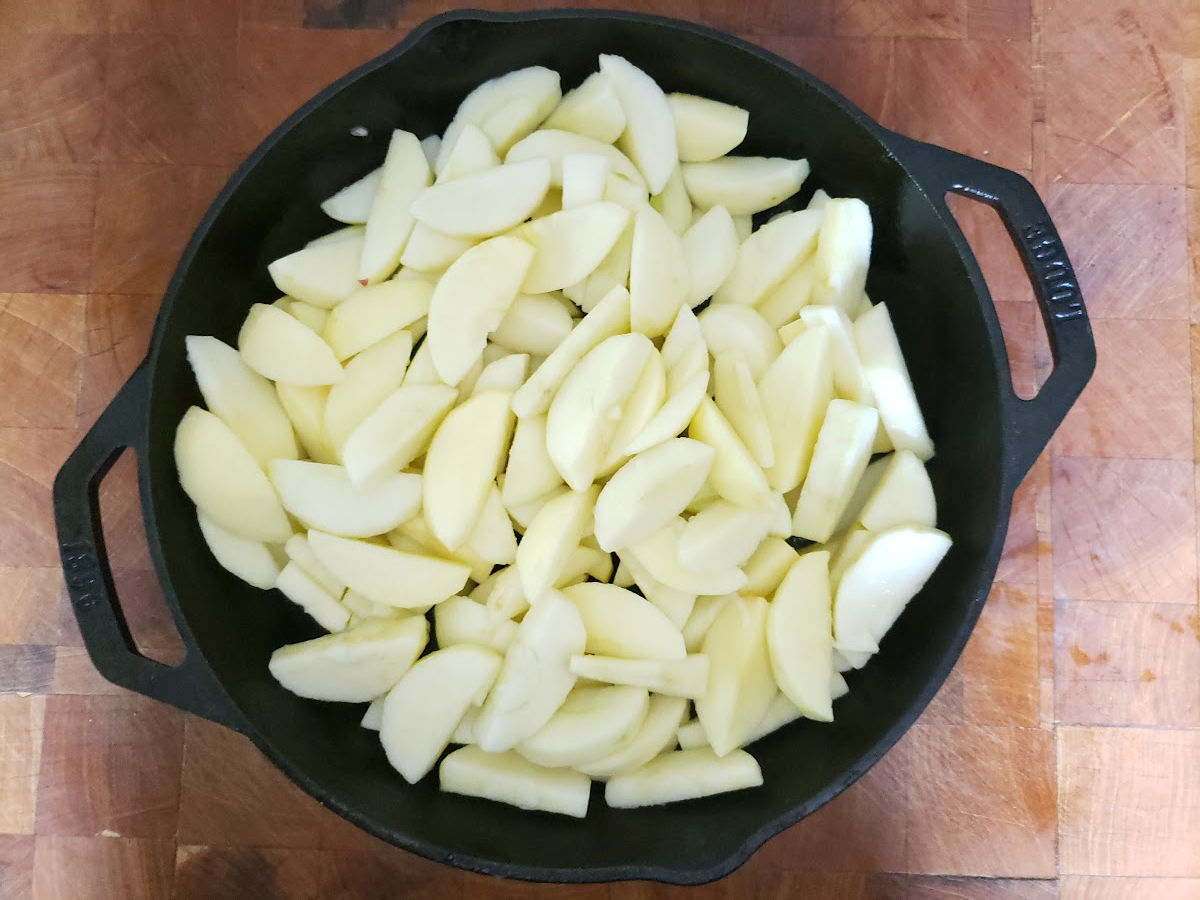Apple slices in dual handle cast iron skillet on butcher block.