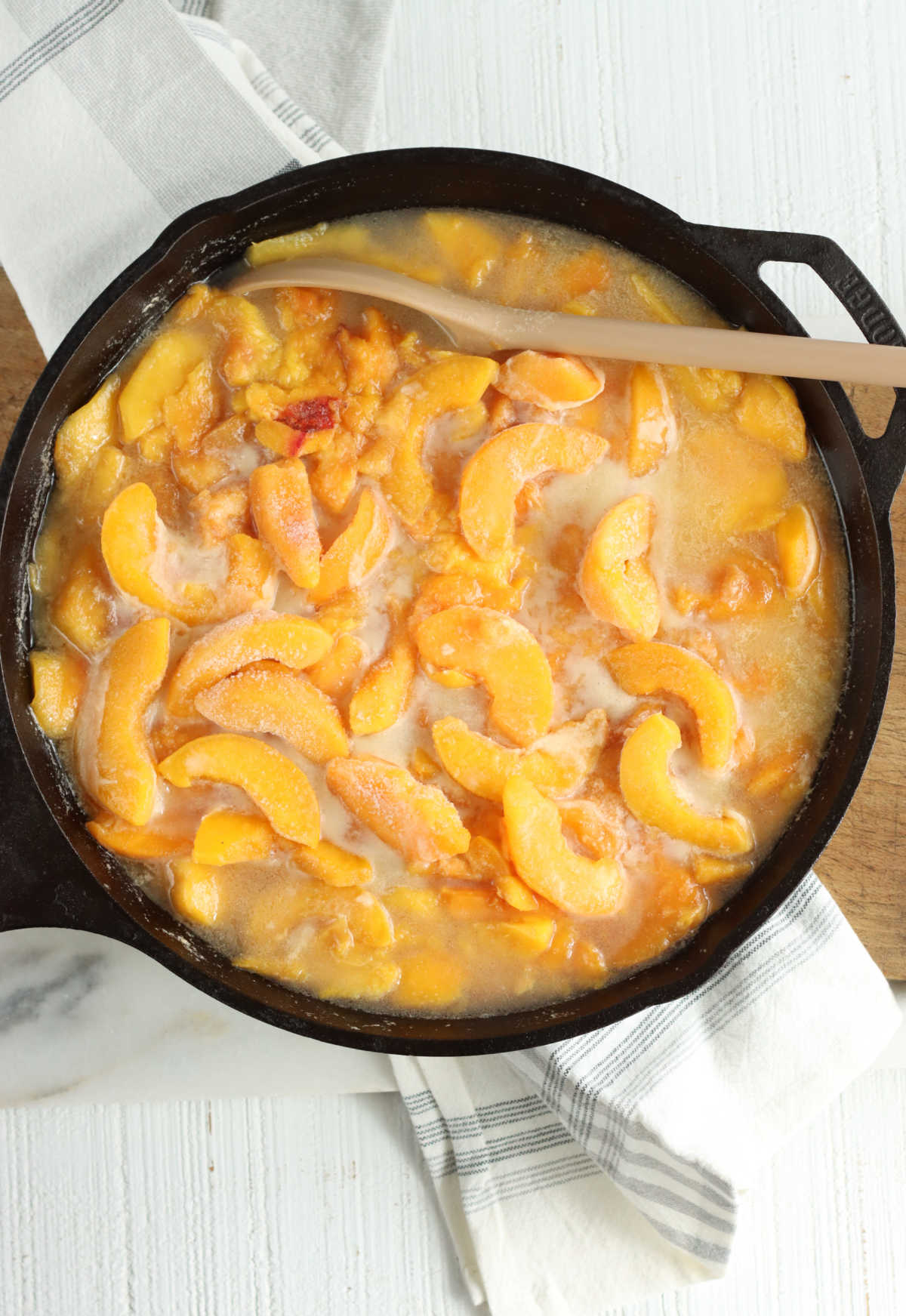 Cast iron skillet with frozen peach slices on white marble.