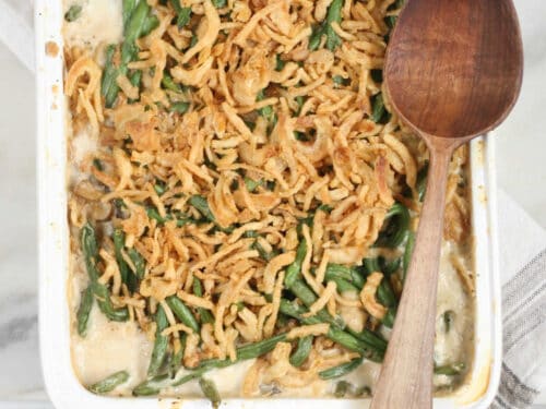 White rectangle baking dish with green bean casserole and wooden spoon.