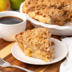 Slice of apple crumb pie on small white plate.