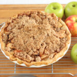 Apple crumble pie on butcher block, red and green apples around.