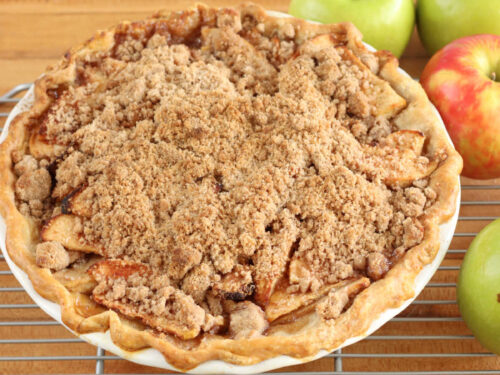 Apple crumble pie on butcher block, red and green apples around.