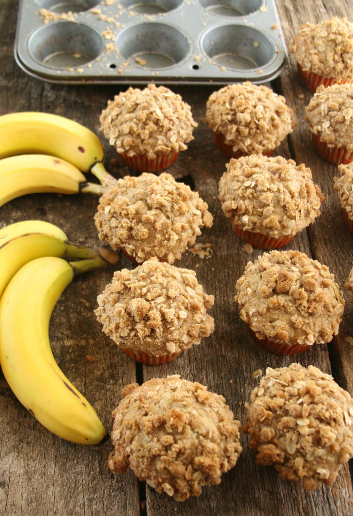Banana muffins with oatmeal topping on reclaimed wood boards, ripe bananas.