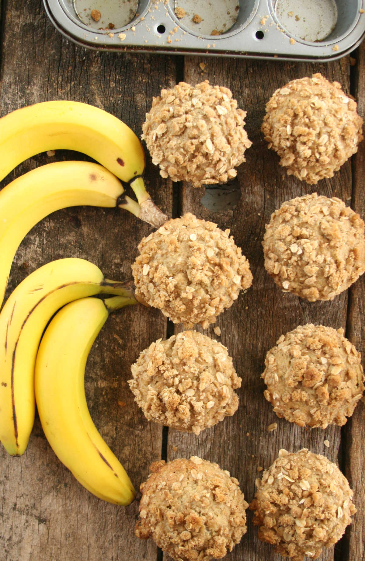 Banana oatmeal muffins on reclaimed wood boards, ripe bananas to left.