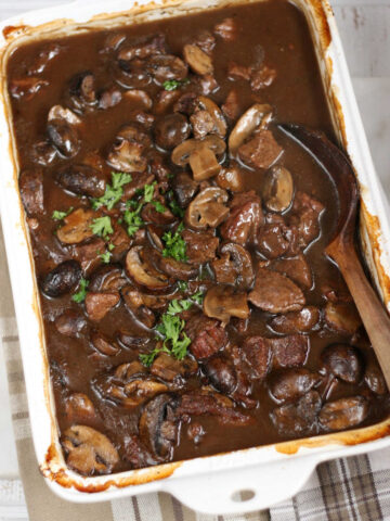 Stew beef and brown gravy in white rectangle baking dish, wooden spoon.