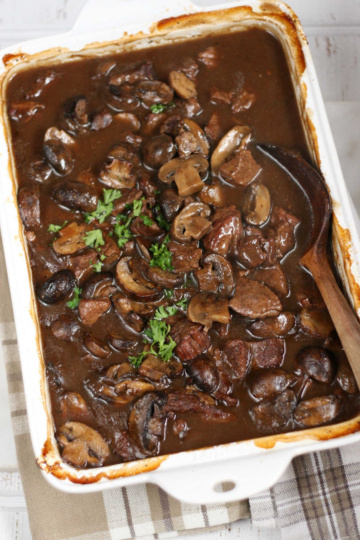 Stew beef and brown gravy in white rectangle baking dish, wooden spoon.