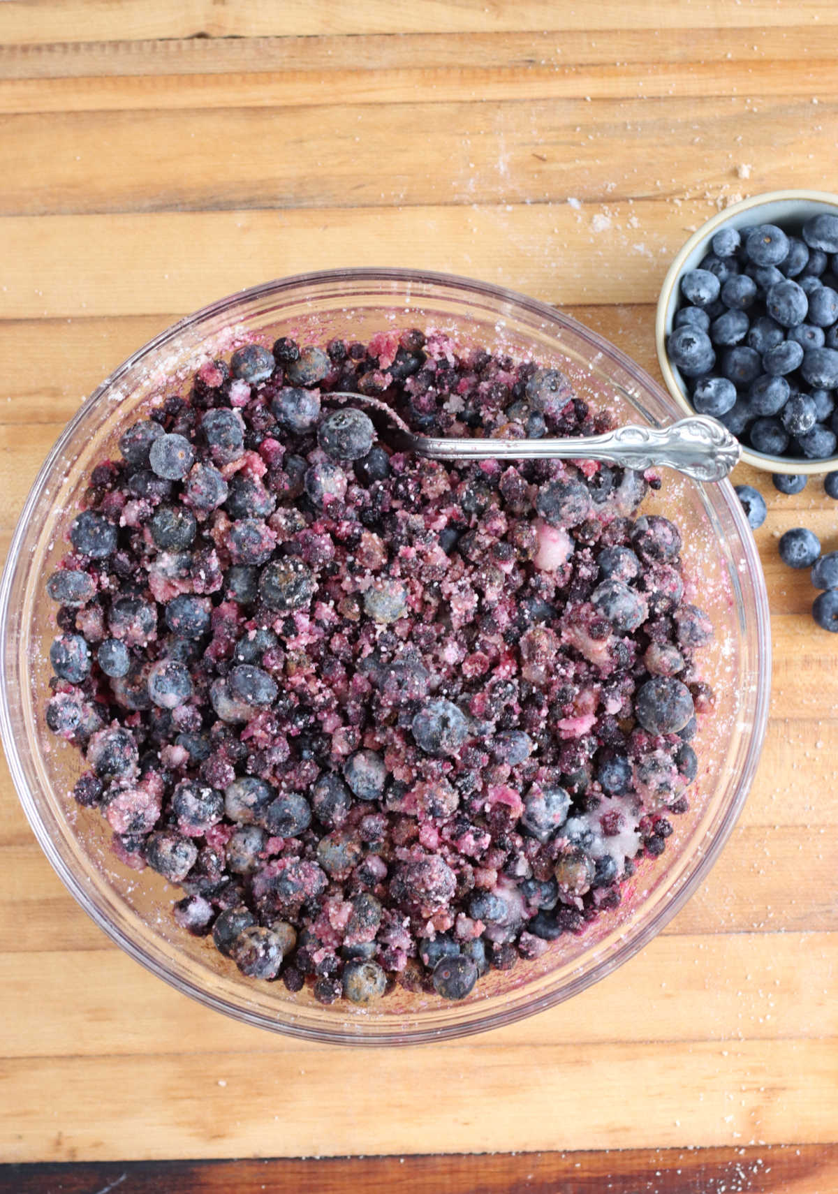 Frozen blueberries with sugar, tapioca in clear glass bowl on butcher block.