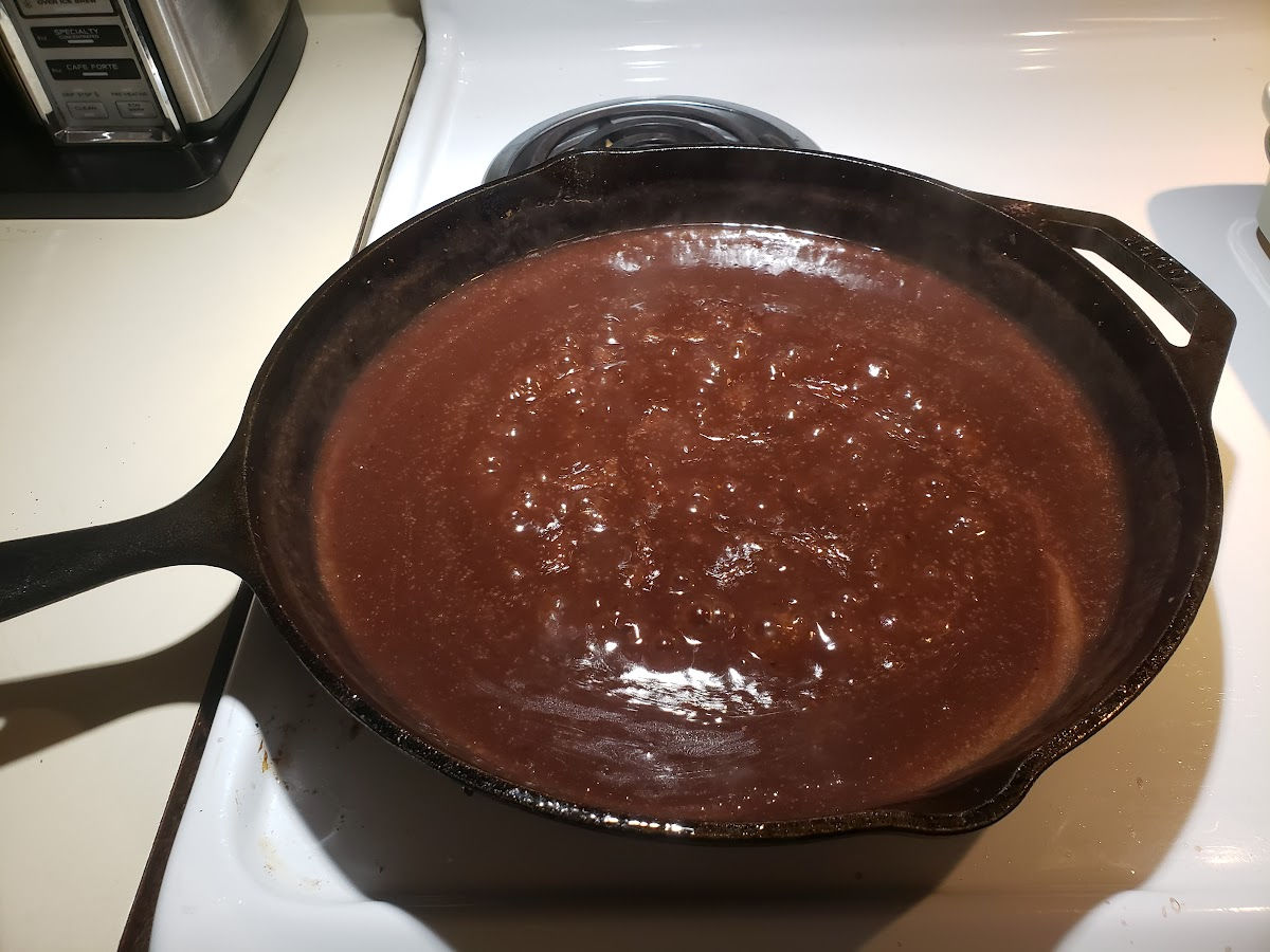 Making brown gravy in large cast iron skillet on white kitchen stove.